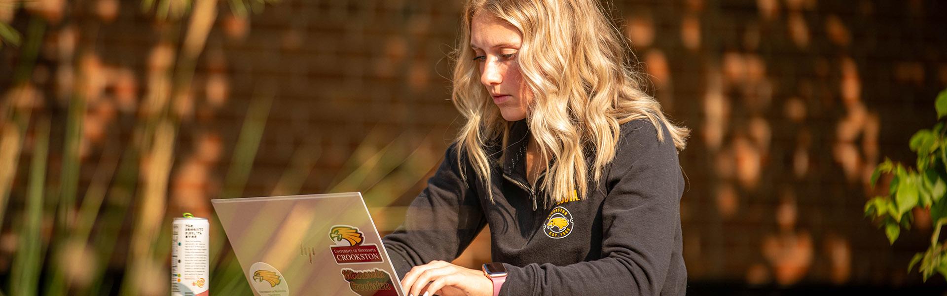 Female student sitting outside on her laptop during the fall