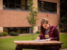 Student sitting outside at a picnic table writing