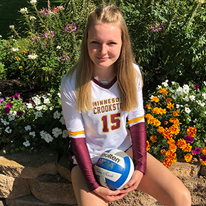 Lauren Wallace, senior Golden Eagle volleyball sitting with a volleyball by the flowers.