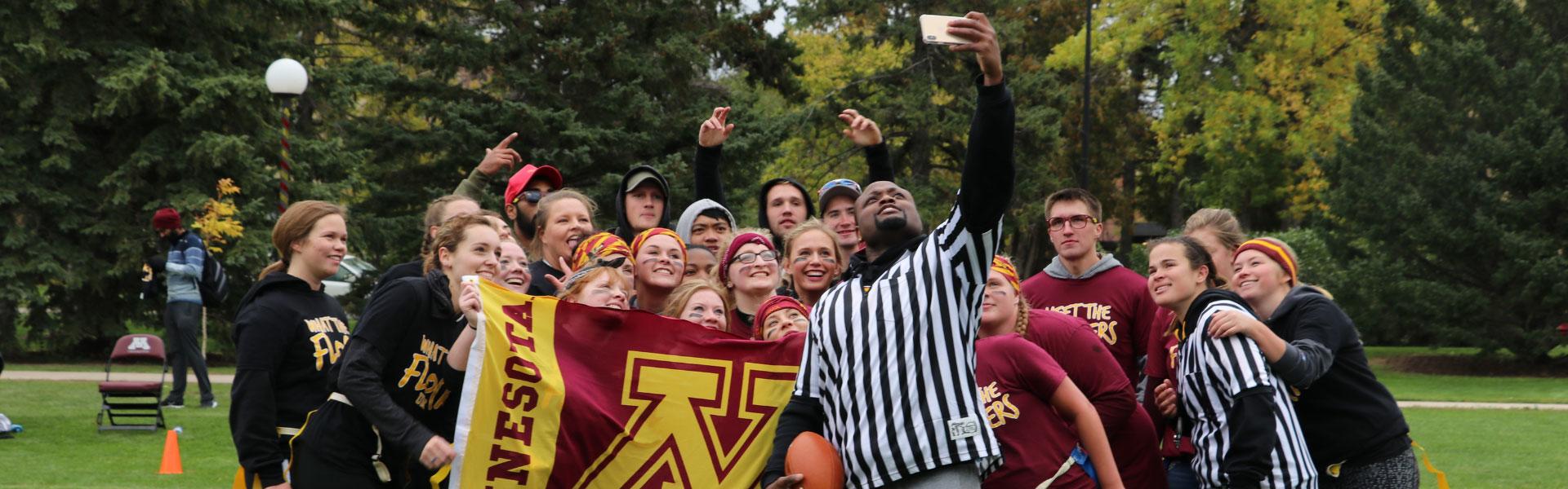 A group of students playing powder puff football during homecoming pose for a selfie with the referees.