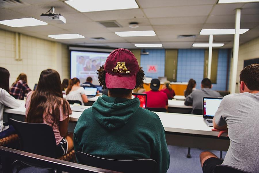 Student sitting in class with a backwards M Crookston logo hat