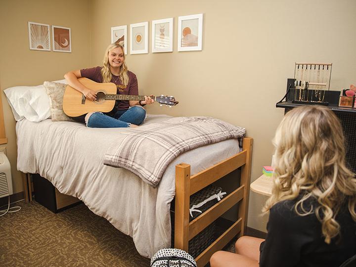 Two female students in a Centennial Hall bedroom with a guitar