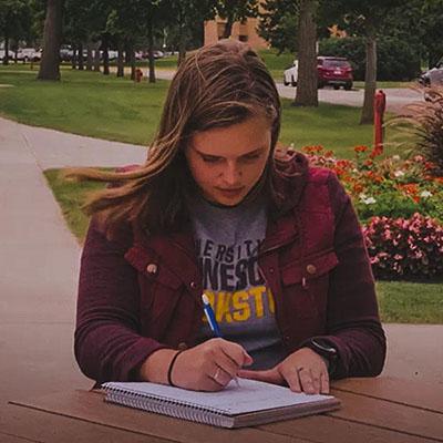 Eleora DeMuth sitting outside Sargeant Student Center at a picnic table writing in a notebook