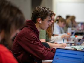 Male student sitting in a U of M Crookston classroom with Airpods and a laptop